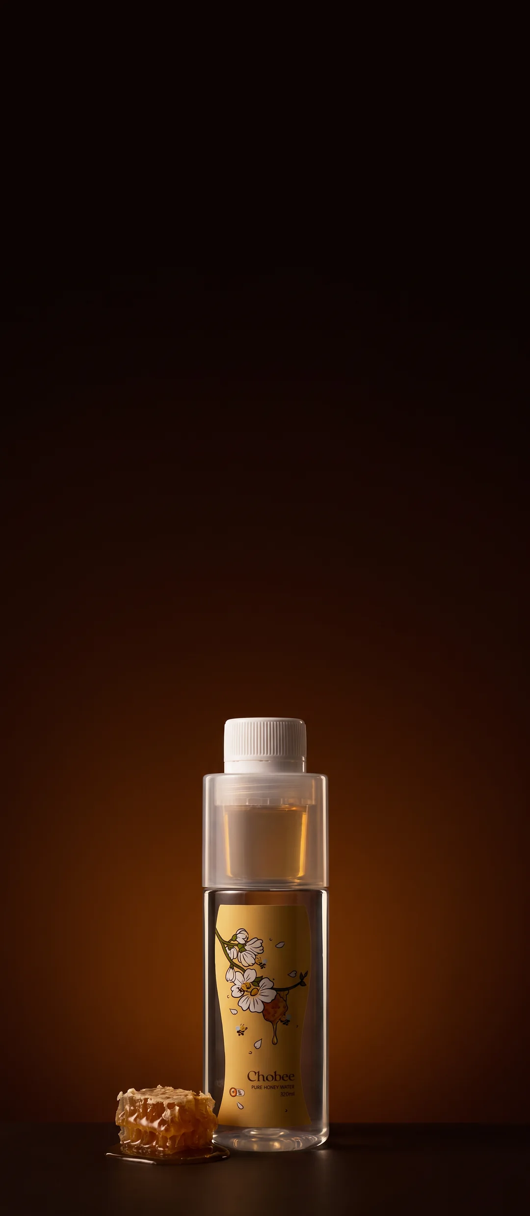Raw honeycomb beside a bottle of CHOBEE Pure Honey Water, lit against a deep amber backdrop